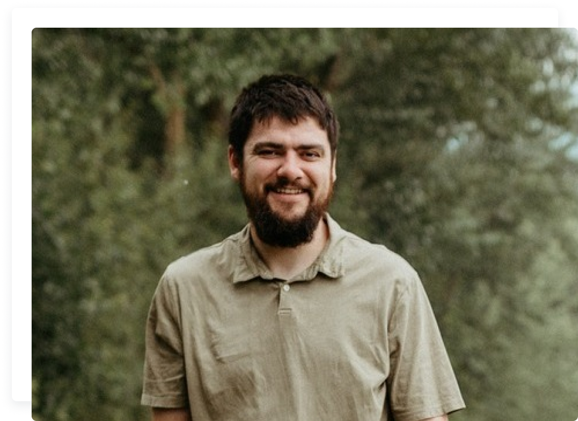 A man with beard and mustache standing in front of trees.