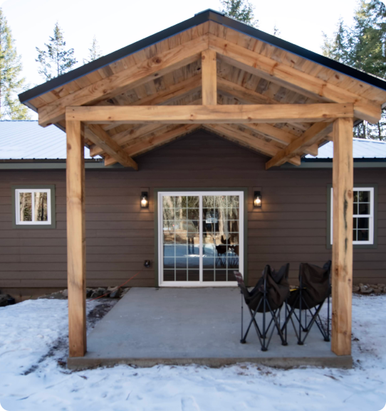 A covered porch with chairs and snow on the ground.